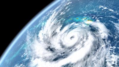 Satellite view of a swirling hurricane over the ocean with a visible coastline in the top right, showcasing the storm's spiral cloud formation.